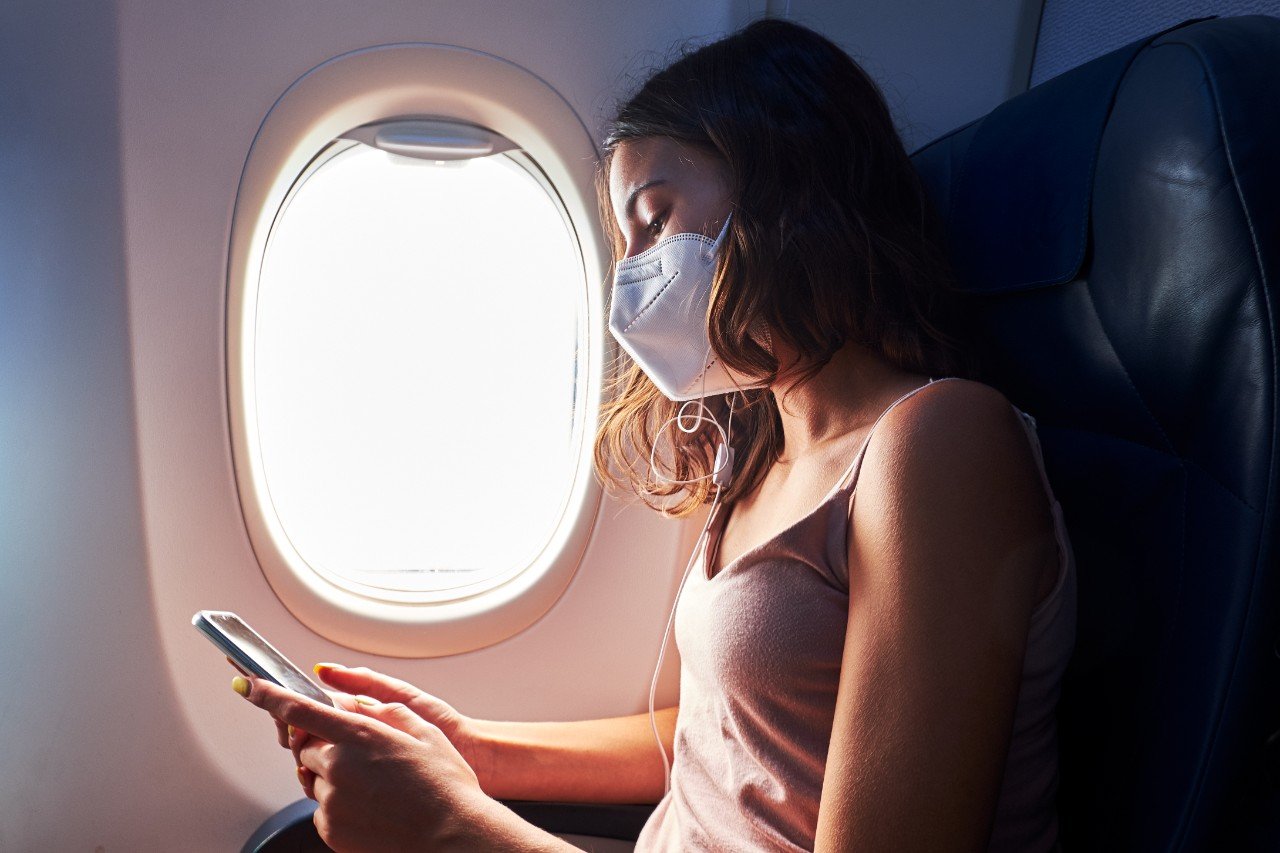 Young girl wearing face mask using smartphone while traveling on airplane