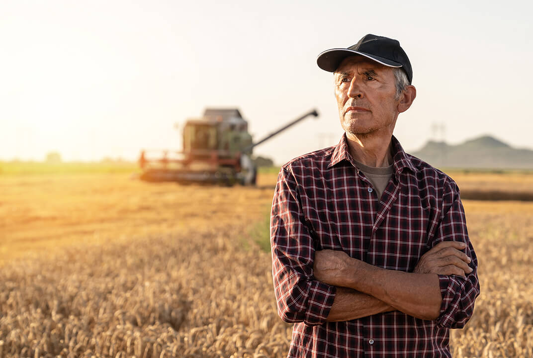 Man stood in field in front of combine harvester with sun setting in background