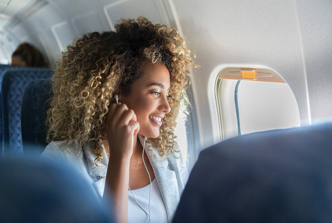 Woman in an aircraft inserting headphones into ears whilst looking out of the window