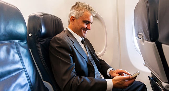 middle aged businessman using cell phone on airplane
