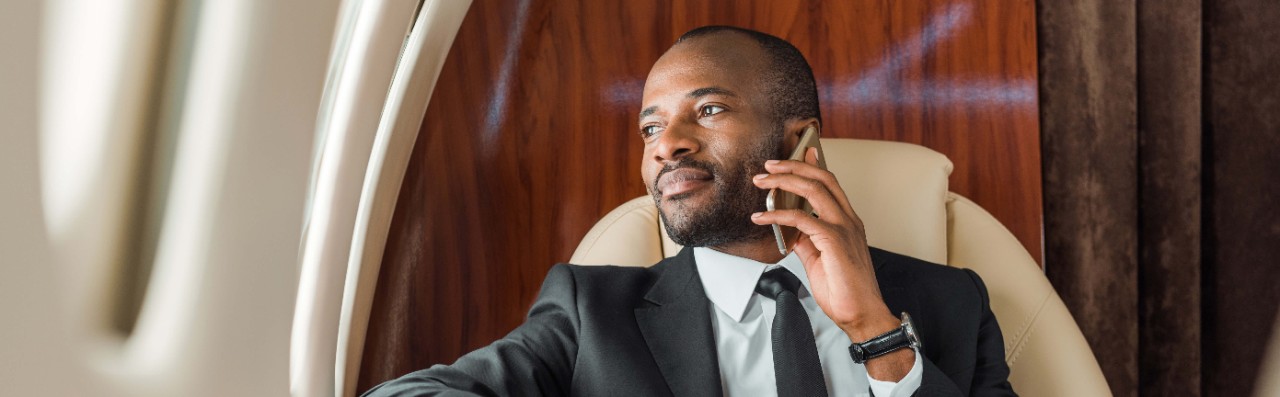 Panoramic shot of handsome African American businessman talking on smartphone in private jet 