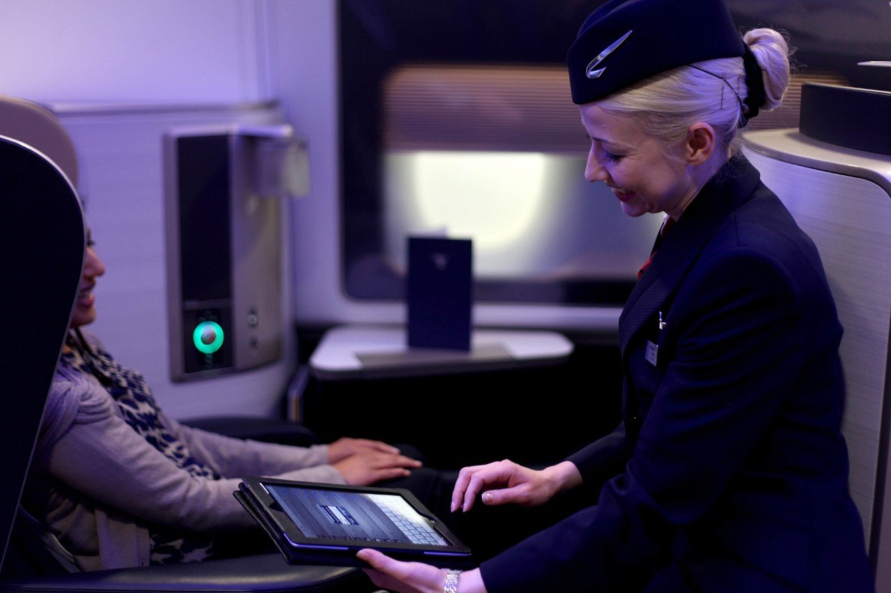 British Airways cabin crew speaking to a customer onboard taking an order using a tablet