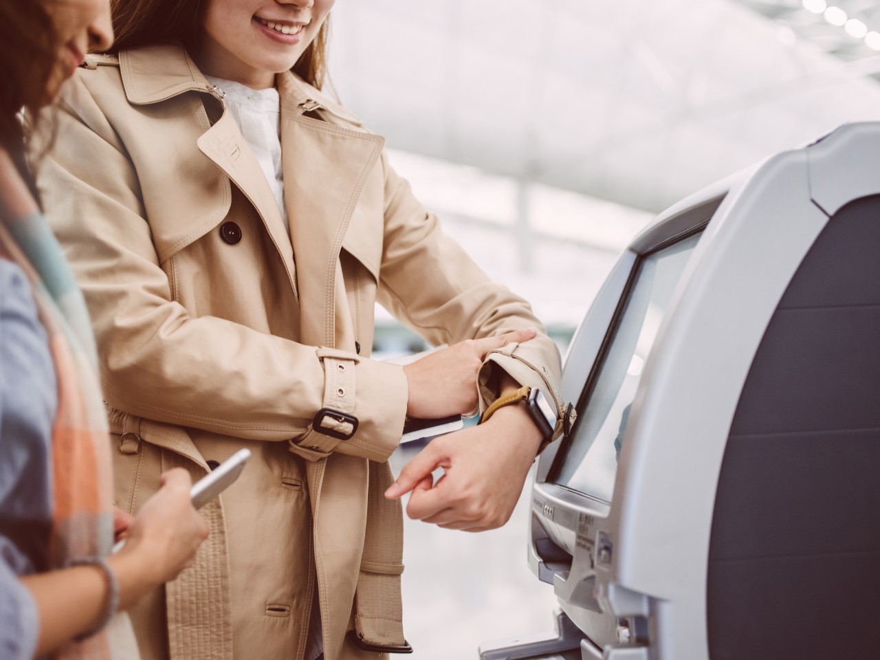 Two women connecting the smart watch to the self-check in kiosk at the airport
