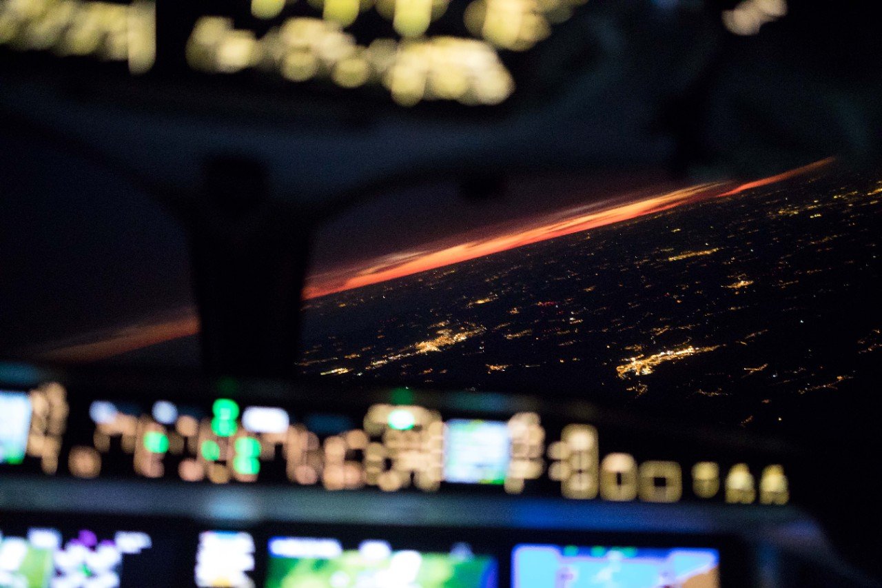 View from a commercial airliner cockpit looking out at a sunset as they bank whilst flying over an urban area