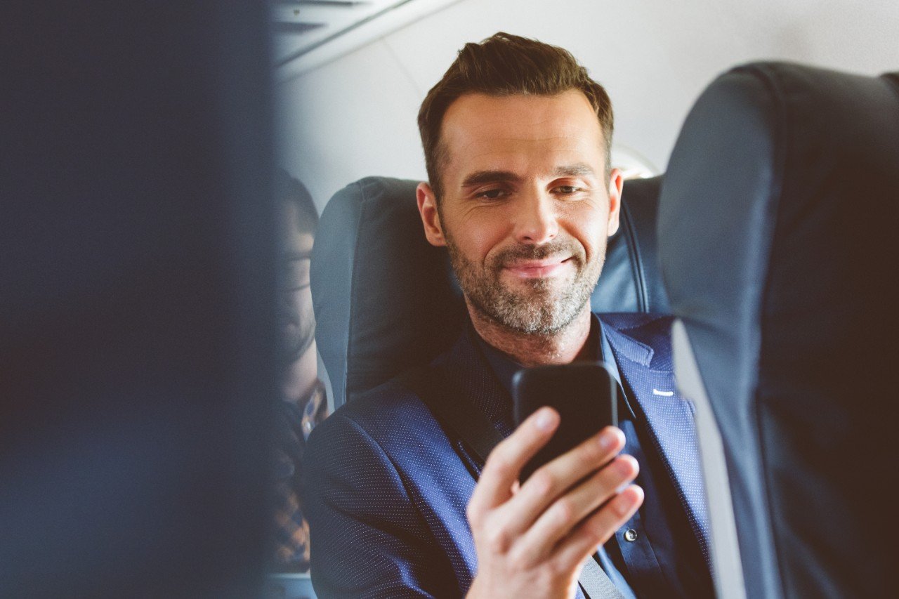 Happy male passenger with smart phone during flight.
