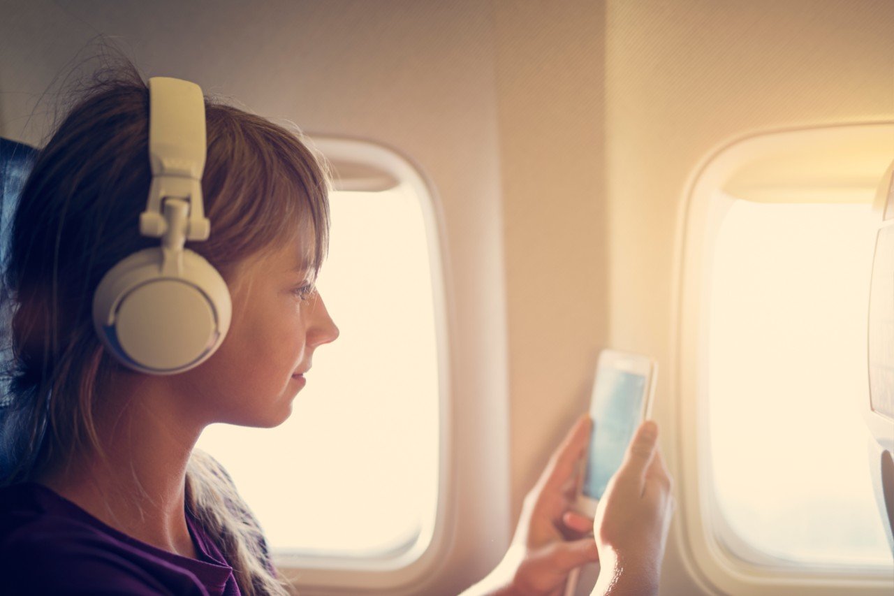 Teenage girl sitting on a plane and using her mobile smartphone