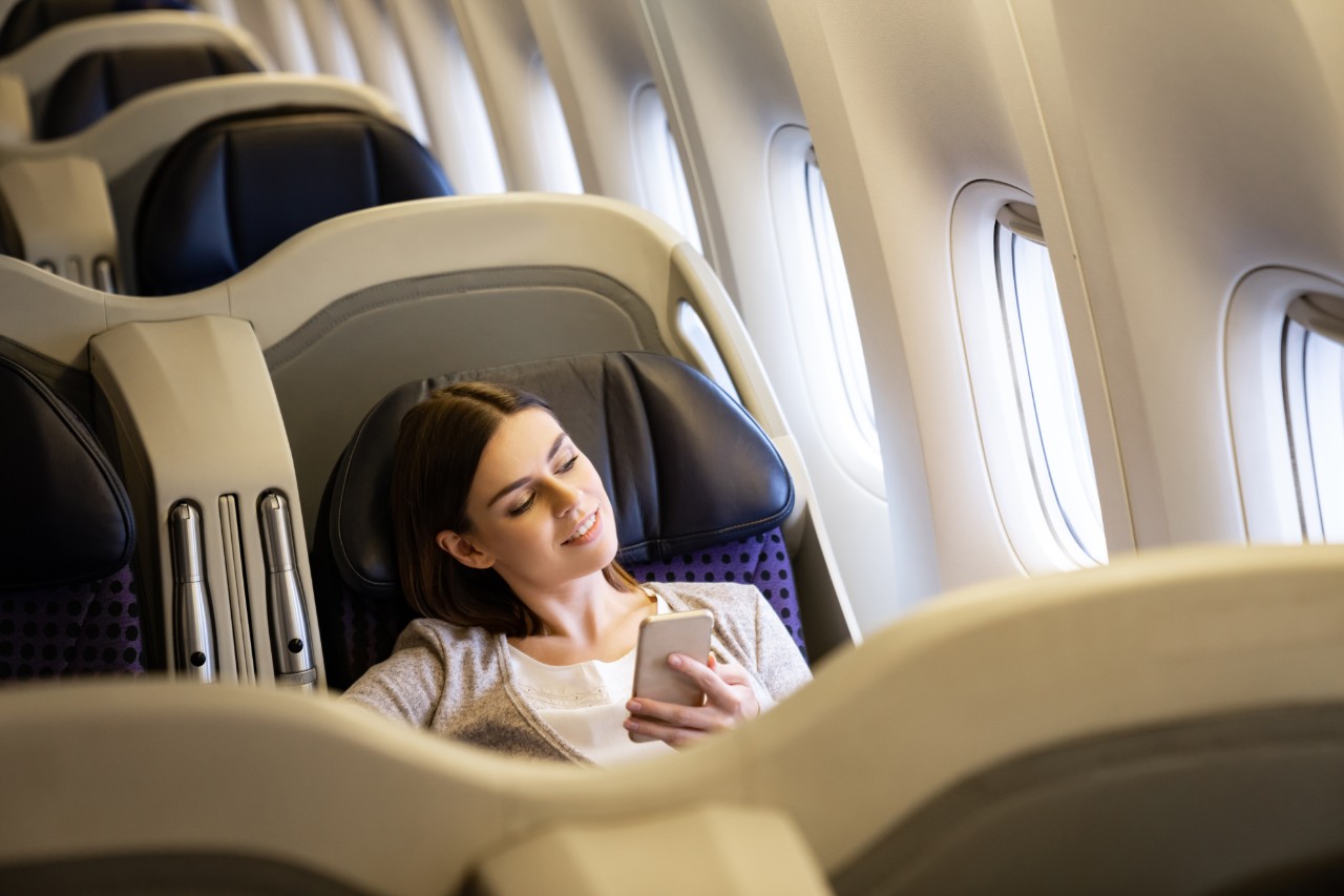 Happy woman traveling by plane and using her cell phone onboard in business class