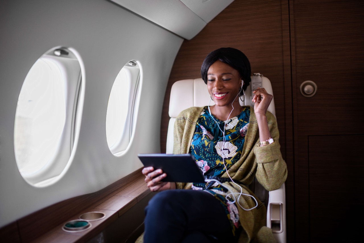 Woman sitting inside private jet airplane and holding tablet device