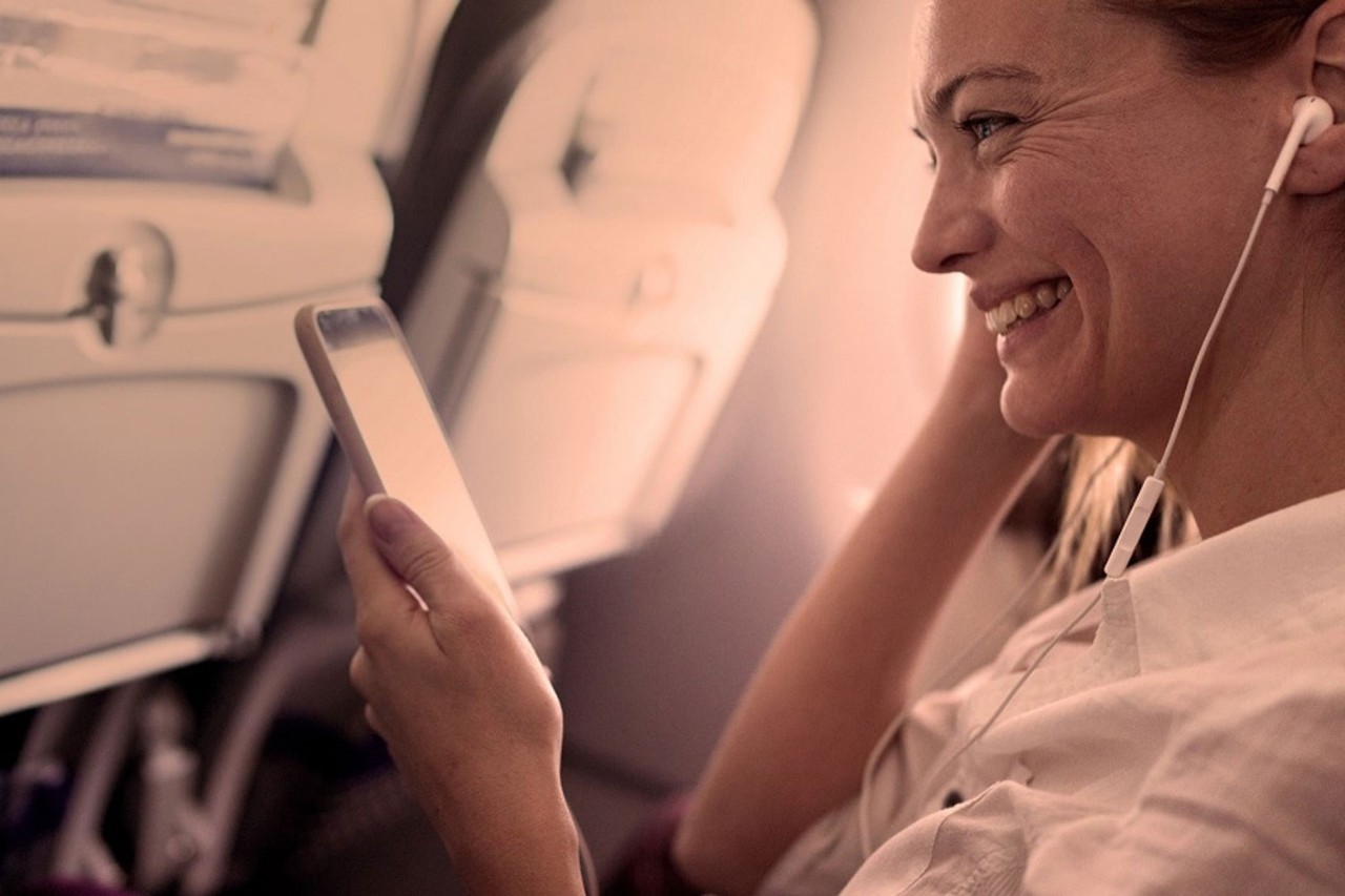 Woman using a smartphone in economy enjoying being connected to Inmarsat In-Flight Connectivity 