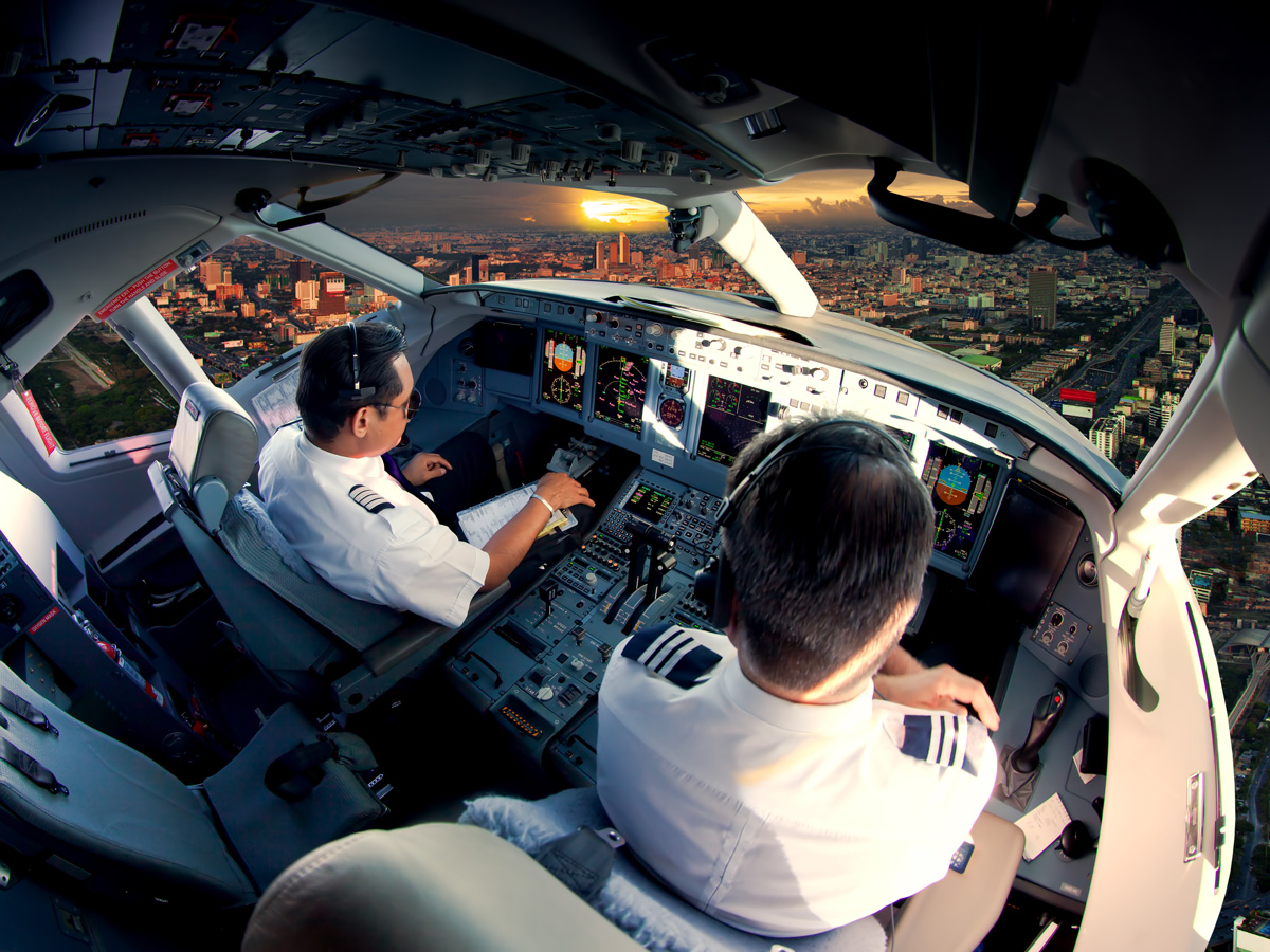 Pilots coming into land over busy city in a modern airline cockpit, sun setting behind the skyline