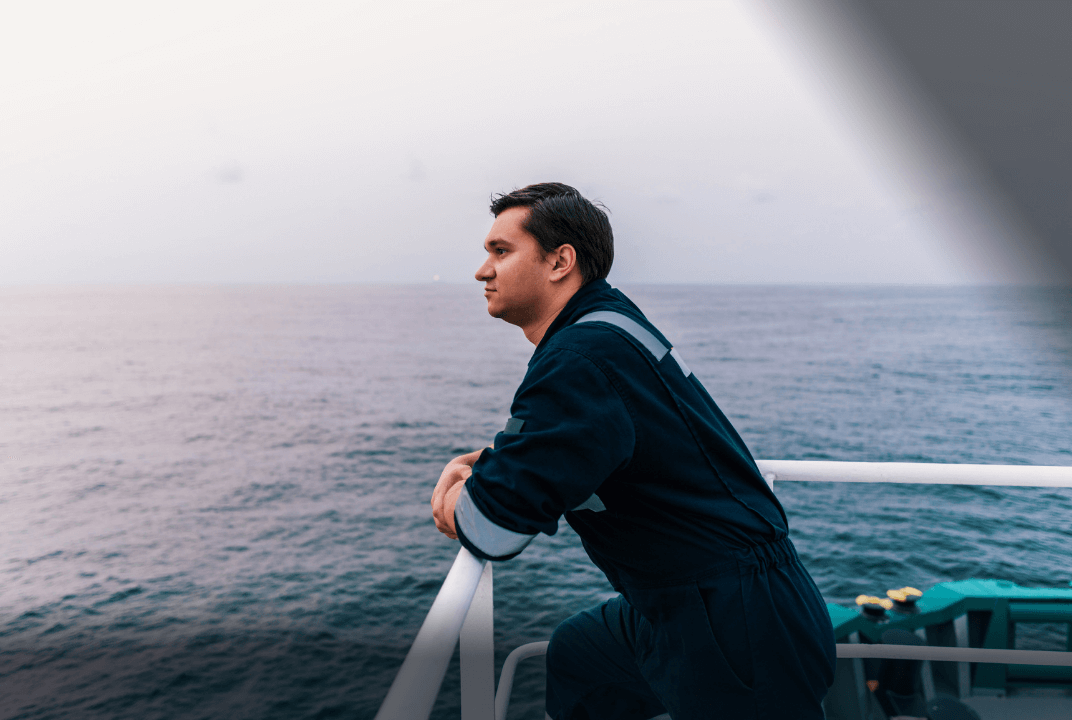 Male seafarer leaning on the rail of ship staring out to sea