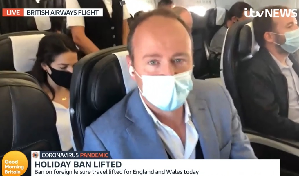 Male news reporter seated on a plane wearing a mask and live broadcasting to ITV's Good Morning Britain