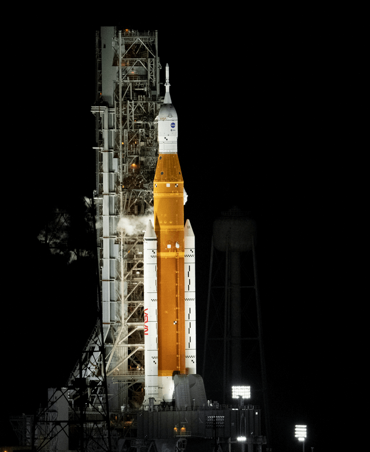 Large rocket stands upright on a launch pad, ready for launch, at night time
