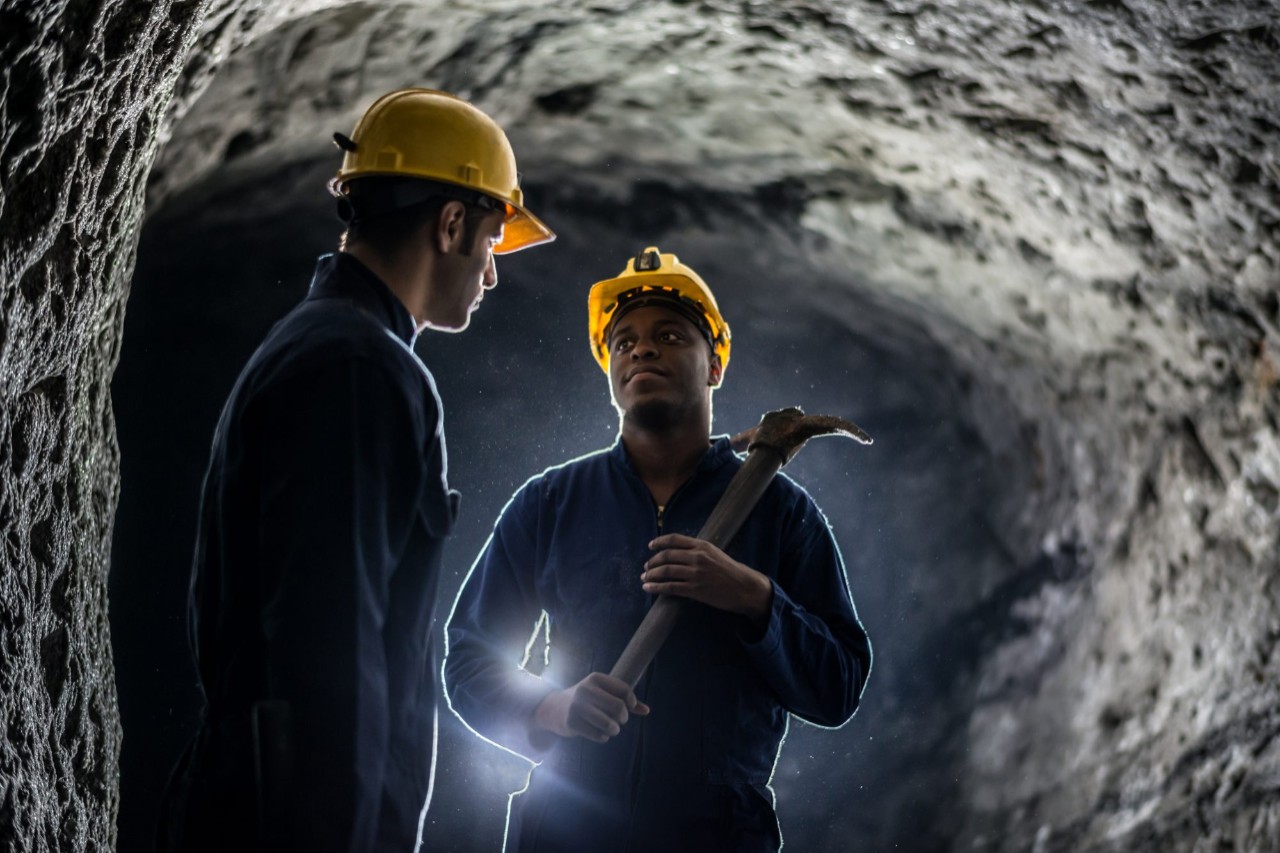 Miners working at a mine wearing helmets and holding tools
