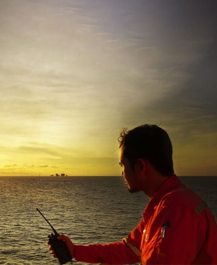 Seafarer at sea holds phone and looks out to the horizon as the sun sets