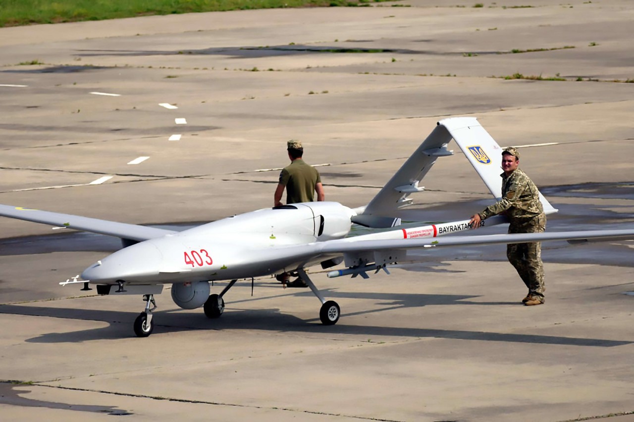 large UAV on the runway next to two military uniformed men