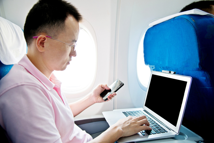 Man using smart phone and laptop on airplane.