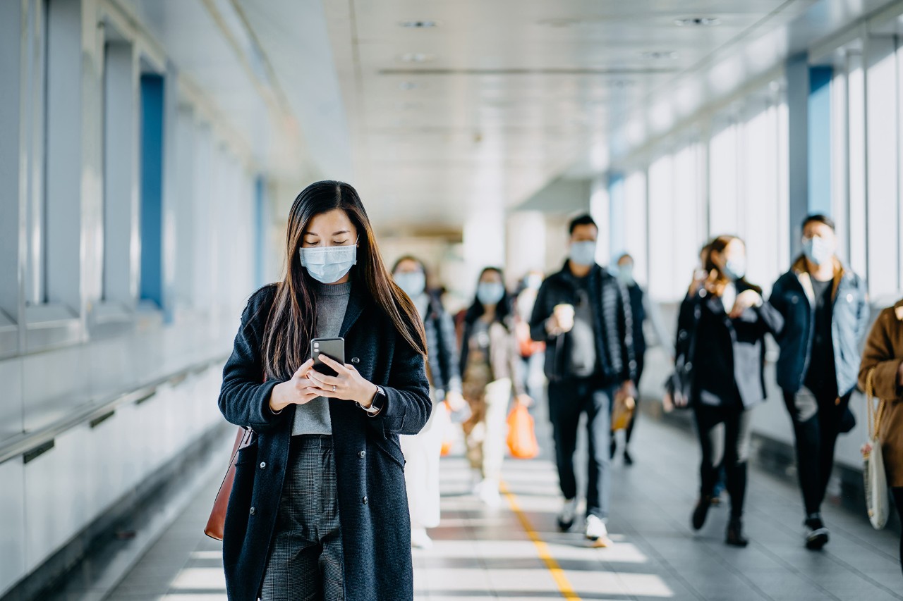 Woman in mask using her mobile phone whilst moving through an airport