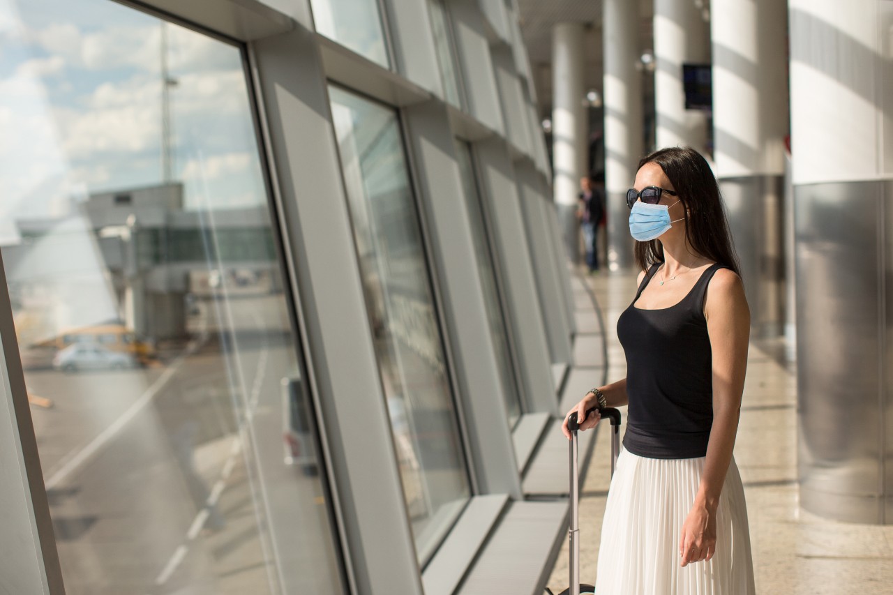 Woman wearing a mask for protection against Coronavirus with baggage in international airport.