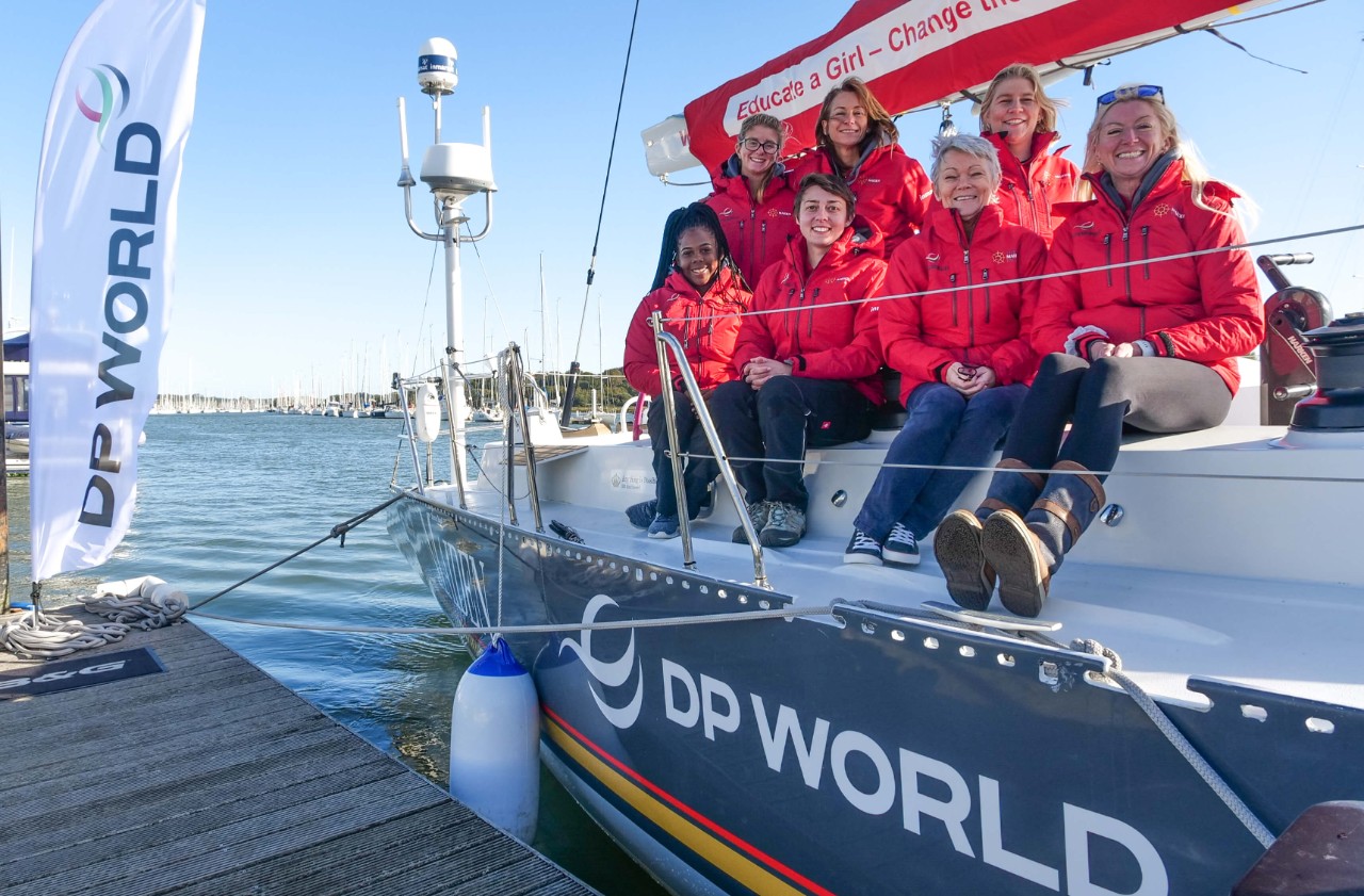 Seven women, including Tracy Edwards, sitting on the deck of Maiden sailing boat, docked by a jetty
