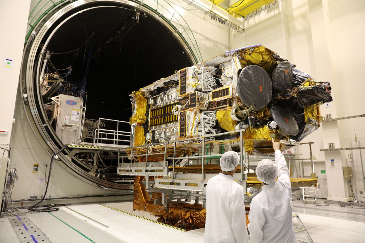 large satellite entering a tunnel chamber with two technicians in lab coats