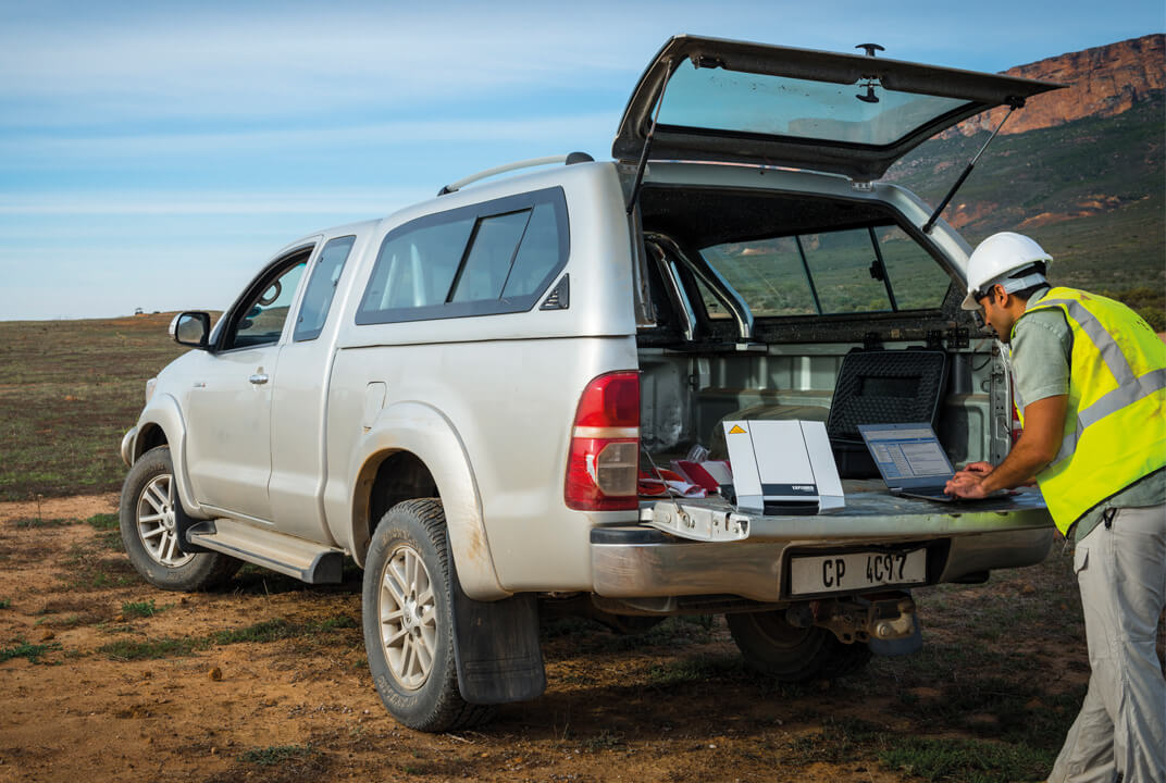 Worker using a laptop and Inmarsat connectivity from the back of a pick up truck