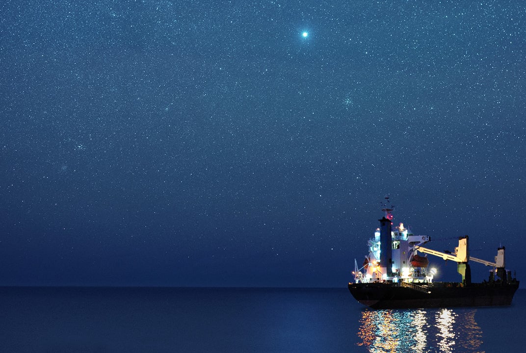Ship illuminated by onboard lights, reflecting on a still ocean at night