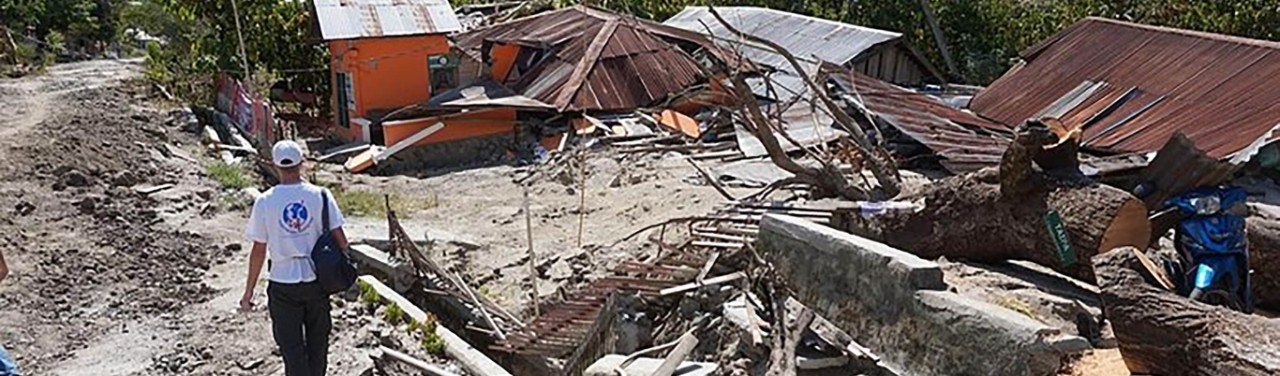 Télécoms Sans Frontières member walking through a residential area recently suffering from a disaster with collapsed buildings around them.